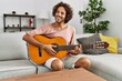 © Krakenimages.com - Young hispanic man smiling happy playing classical guitar sitting on the sofa at home.