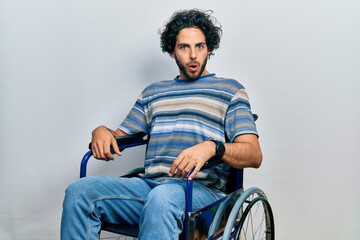 Wall Mural - Handsome hispanic man sitting on wheelchair in shock face, looking skeptical and sarcastic, surprised with open mouth