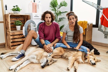 Wall Mural - Young hispanic couple doing laundry with dogs afraid and shocked with surprise and amazed expression, fear and excited face.