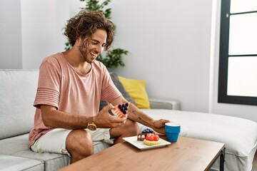 Canvas Print - Young hispanic man having breakfast sitting on the sofa at home.