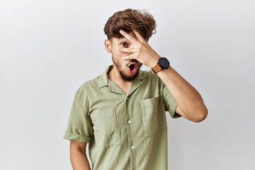 Wall Mural - Young arab doctor man standing over isolated background peeking in shock covering face and eyes with hand, looking through fingers with embarrassed expression.