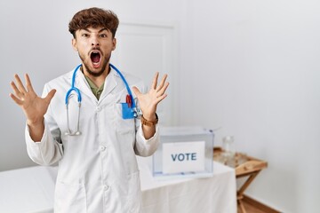 Wall Mural - Young arab doctor man at political election by ballot crazy and mad shouting and yelling with aggressive expression and arms raised. frustration concept.