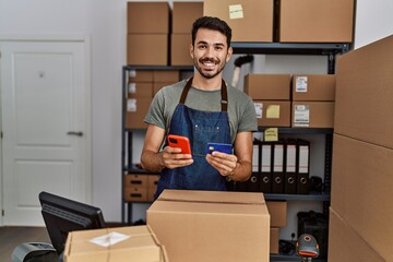 Wall Mural - Young hispanic man business worker using smartphone and credit card at storehouse