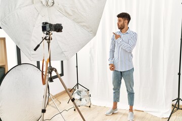 Canvas Print - Arab young man posing as model at photography studio surprised pointing with finger to the side, open mouth amazed expression.