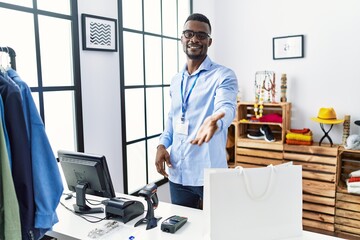 Wall Mural - Young african man working as manager at retail boutique smiling cheerful offering palm hand giving assistance and acceptance.