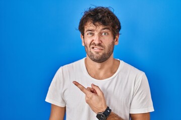 Poster - Hispanic young man standing over blue background pointing aside worried and nervous with forefinger, concerned and surprised expression