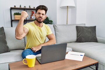 Poster - Young man with beard using laptop at home angry and mad raising fist frustrated and furious while shouting with anger. rage and aggressive concept.