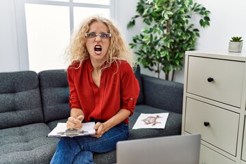 Poster - Middle age psychologist woman at consultation office angry and mad screaming frustrated and furious, shouting with anger. rage and aggressive concept.