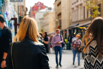 Defocus two stylish blonde and white women walking outdoors in autumn city street at sunset time wearing black jacket. View from the back. Friendship and travel. Out of focus