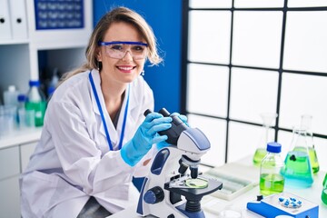 Wall Mural - Young woman scientist smiling confident using microscope at laboratory