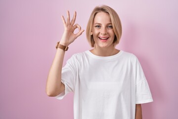 Poster - Young caucasian woman standing over pink background smiling positive doing ok sign with hand and fingers. successful expression.