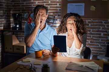 Poster - Middle age hispanic couple using touchpad sitting on the table at night yawning tired covering half face, eye and mouth with hand. face hurts in pain.