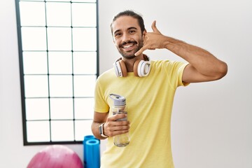 Canvas Print - Young hispanic man wearing sportswear and drinking water at the gym smiling doing phone gesture with hand and fingers like talking on the telephone. communicating concepts.