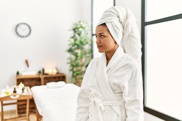 Young brunette woman wearing towel and bathrobe standing at beauty center looking to side, relax profile pose with natural face with confident smile.