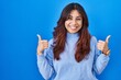 Leinwandbild Motiv Hispanic young woman standing over blue background success sign doing positive gesture with hand, thumbs up smiling and happy. cheerful expression and winner gesture.