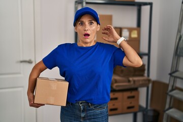 Poster - Middle age brunette woman working wearing delivery uniform and cap crazy and scared with hands on head, afraid and surprised of shock with open mouth