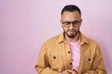 Wall Mural - Young hispanic man standing over pink background with hand on stomach because nausea, painful disease feeling unwell. ache concept.