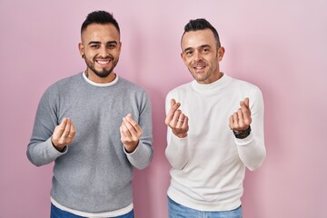 Sticker - Homosexual couple standing over pink background doing money gesture with hands, asking for salary payment, millionaire business