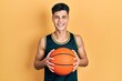 © Krakenimages.com - Young hispanic man holding basketball ball smiling with a happy and cool smile on face. showing teeth.