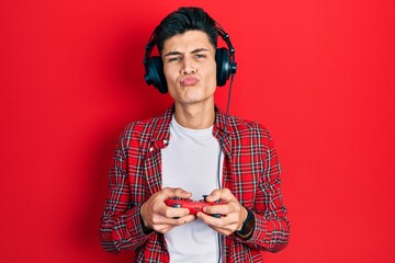 Canvas Print - Young hispanic man playing video game holding controller looking at the camera blowing a kiss being lovely and sexy. love expression.