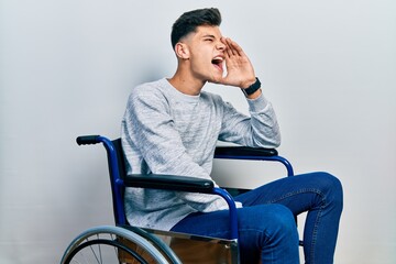 Canvas Print - Young hispanic man sitting on wheelchair shouting and screaming loud to side with hand on mouth. communication concept.