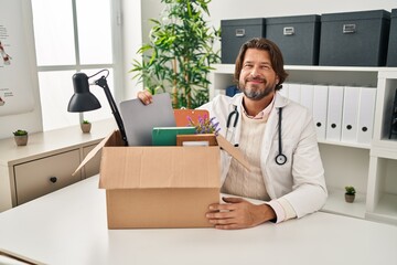 Sticker - Handsome middle age doctor man holding box with items relaxed with serious expression on face. simple and natural looking at the camera.