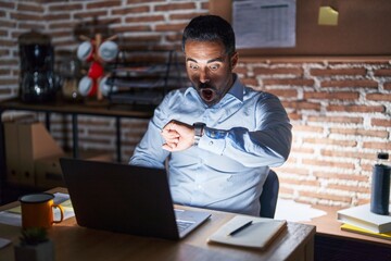 Wall Mural - Hispanic man with beard working at the office at night looking at the watch time worried, afraid of getting late