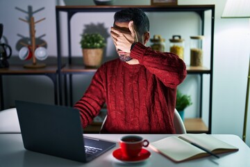 Sticker - Young hispanic man with beard using computer laptop at night at home covering eyes with hand, looking serious and sad. sightless, hiding and rejection concept