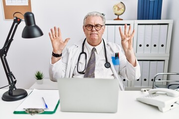 Wall Mural - Senior caucasian man wearing doctor uniform and stethoscope at the clinic showing and pointing up with fingers number nine while smiling confident and happy.