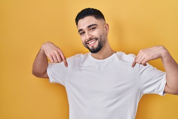 Canvas Print - Young handsome man wearing casual t shirt over yellow background looking confident with smile on face, pointing oneself with fingers proud and happy.