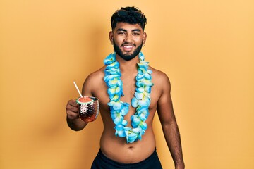 Poster - Arab man with beard wearing swimsuit and hawaiian lei drinking cocktail looking positive and happy standing and smiling with a confident smile showing teeth