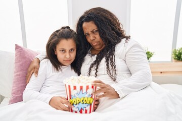 Sticker - Mother and young daughter eating popcorn in the bed skeptic and nervous, frowning upset because of problem. negative person.