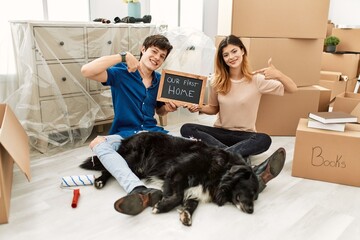 Poster - Young caucasian couple with dog holding our first home blackboard at new house looking confident with smile on face, pointing oneself with fingers proud and happy.