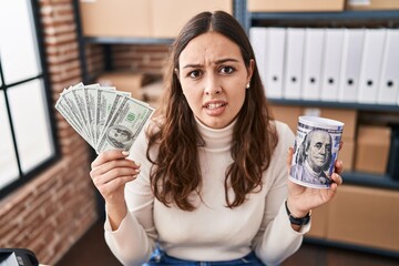 Sticker - Young hispanic woman working at small business ecommerce holding money and piggy bank clueless and confused expression. doubt concept.