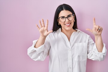 Sticker - Young brunette woman standing over pink background showing and pointing up with fingers number seven while smiling confident and happy.