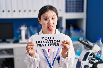 Sticker - Woman with down syndrome working at scientist laboratory holding your donation matters banner sticking tongue out happy with funny expression.