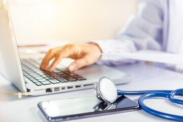 Closeup of doctor or nurse woman in uniform with stethoscope typing information of patient prescription from paperwork medical history form into laptop computer for record document data report