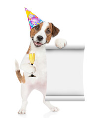 Poster - Happy Jack russell terrier puppy wearing a party cap holds glass of champagne and empty list. isolated on white background