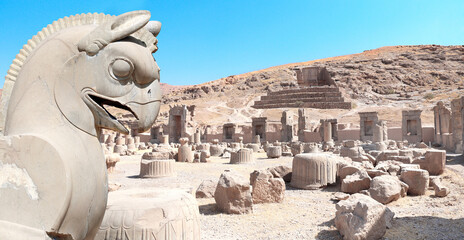 Canvas Print - Stone sculpture of griffin and Ruins of Palace of 100 columns and tomb of Artaxerxes III, Persepolis, Iran