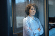 © Westend61 - Thoughtful businesswoman standing with arms crossed seen through glass