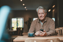 Smiling Senior Man With Mobile Phone In Cafe