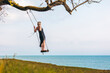 © Westend61 - Mature woman balancing on swing in front of sky