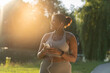 © gpointstudio - African American woman using mobile phone and earphones before exercising at the park in a  summer day