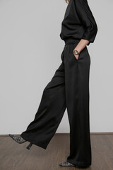 Serie of studio photos of young female model wearing all black classic basic outfit, silk satin blouse and wide legged trousers.