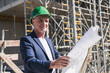 © Westend61 - Smiling architect with blueprint standing at construction site