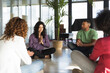 © Westend61 - Businesswoman sitting with hands clasped by colleagues meditating in office