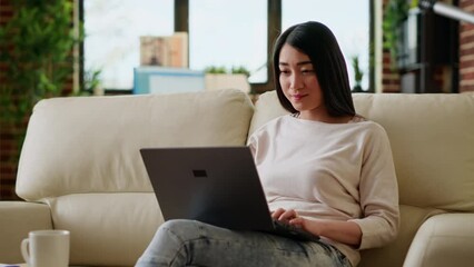 Poster - Smiling office worker at home working remotely on laptop while sitting on sofa in living room. Young adult person doing remote work on modern portable computer while at home.