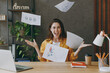 © ViDi Studio - Young fun excited happy successful employee business woman 20s she wear casual yellow shirt throw up paper account documents sit work at wooden office desk with pc laptop. Achievement career concept.