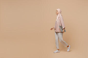 Wall Mural - Full body side view happy young arabian asian muslim woman she wear abaya hijab pink clothes hold closed laptop pc computer isolated on plain light beige background People uae islam religious concept.