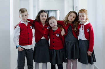 Poster - Happy schoolgrirl with Down syndrome standing with her classmates in school corridor, looking at camera.